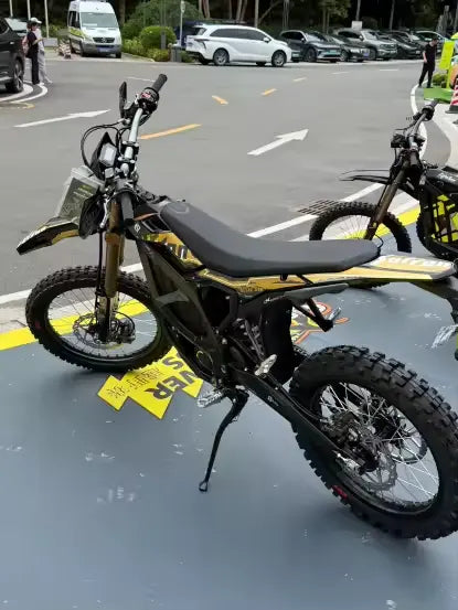 2026 Sur-Ron Ultra Bee HP 24.5kW electric dirt bike in gold graphics parked outdoors at factory facility.
