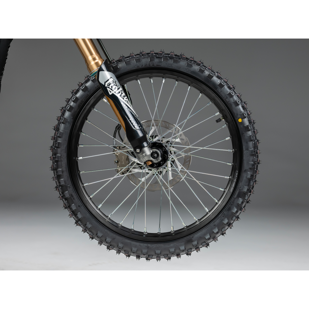 Front wheel detail of 2026 Sur-Ron LBX2 showing heavy-duty off-road spoked wheel, CST knobby tire, hydraulic brake rotor, and gold suspension fork dropouts.