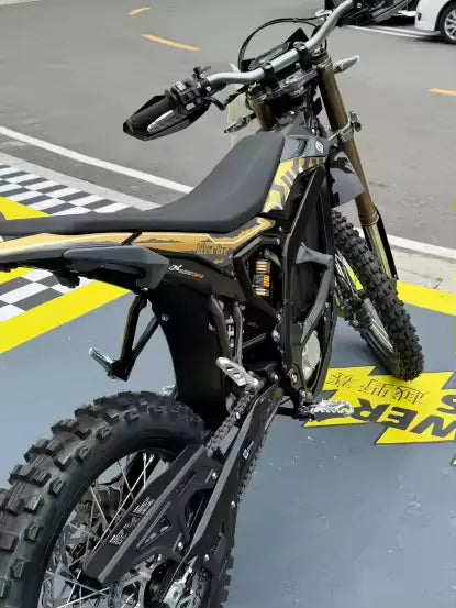 2026 Sur-Ron Ultra Bee HP rear swingarm, chain drive, and off-road knobby tire close-up view at factory floor.