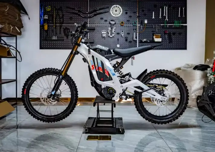 2026 Sur-Ron Light Bee X 10kW electric dirt bike in white side profile view on workshop lift stand.